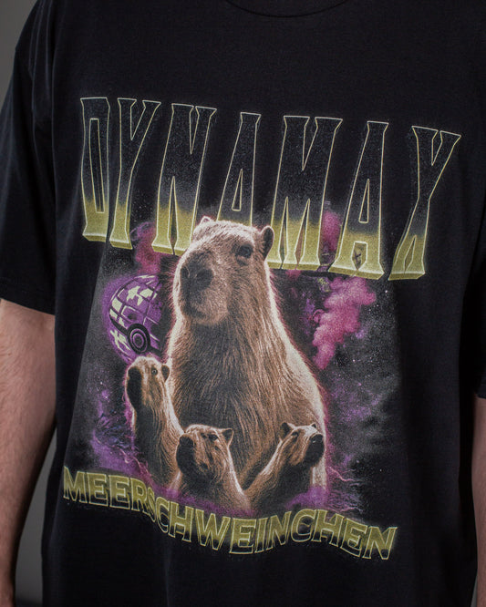 Nahaufnahme des T-Shirts: Zentrale Capybara-Grafik mit leuchtenden Farben, umgeben von kleineren Capybaras, daneben ein violetter Pokéball-ähnlicher Globus; darüber der Text „DYNAMAX“, darunter „MEERSCHWEINCHEN“.