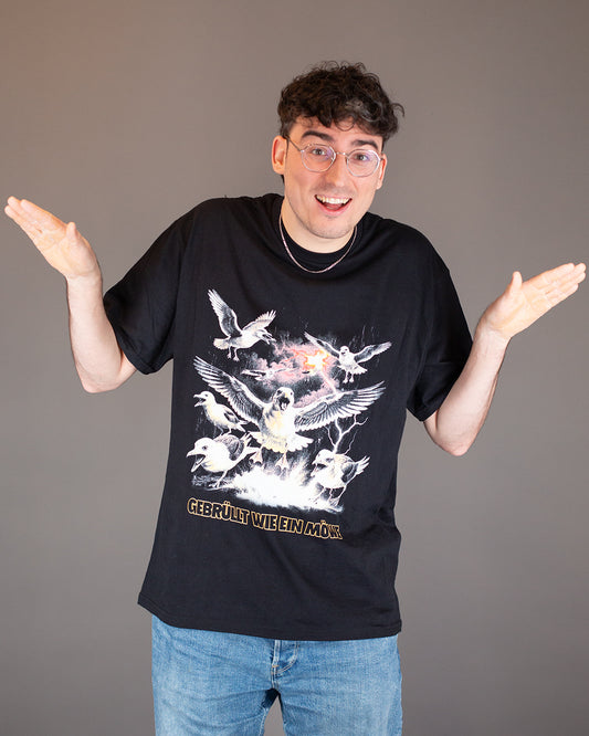 Schwarzes T-Shirt mit großflächigem Frontprint: Eine kreischende Möwe mit ausgebreiteten Flügeln steht im Zentrum eines dramatischen Motivs mit Blitzen, Wolken und weiteren Möwen. Darunter der gelbe Schriftzug: „GEBRÜLLT WIE EIN MÖWE“.
