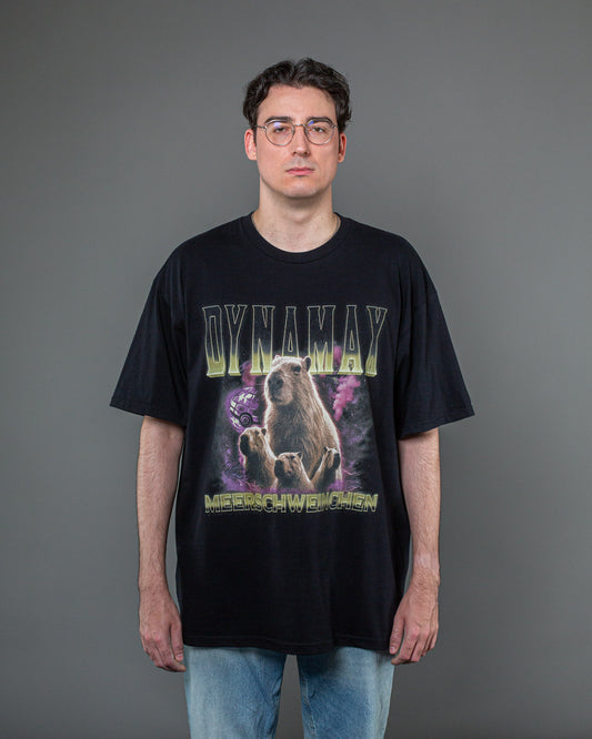 Schwarzes Oversize-T-Shirt mit großflächigem Frontprint einer Capybara-Familie vor violettem Nebel und gelbem „DYNAMAX“-Schriftzug oben sowie „MEERSCHWEINCHEN“ unten.