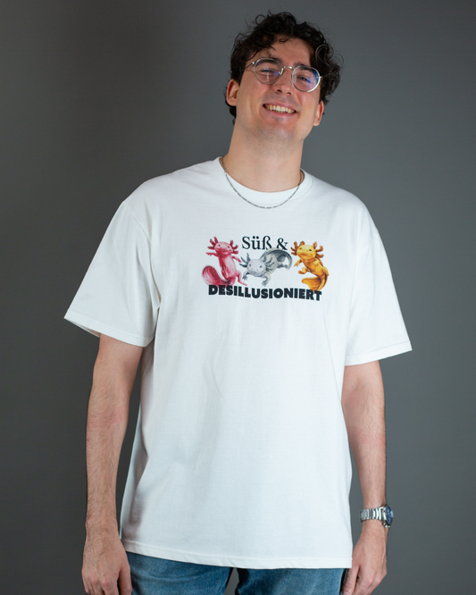 Locker getragenes weißes T-Shirt mit zentralem Print aus drei Axolotl-Figuren in verschiedenen Farben und dem Spruch „Süß & DESILLUSIONIERT“.